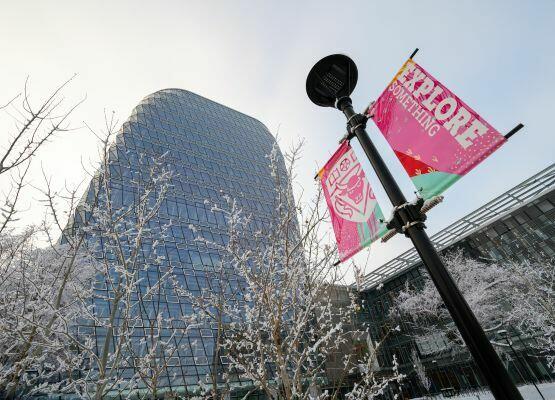 A low angle shot of MacKimmie Tower and Hunter Student Commons with a lamp post, signage, and some trees in view