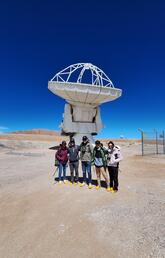 Student researchers pose in front of an ALMA telescope in Chile.